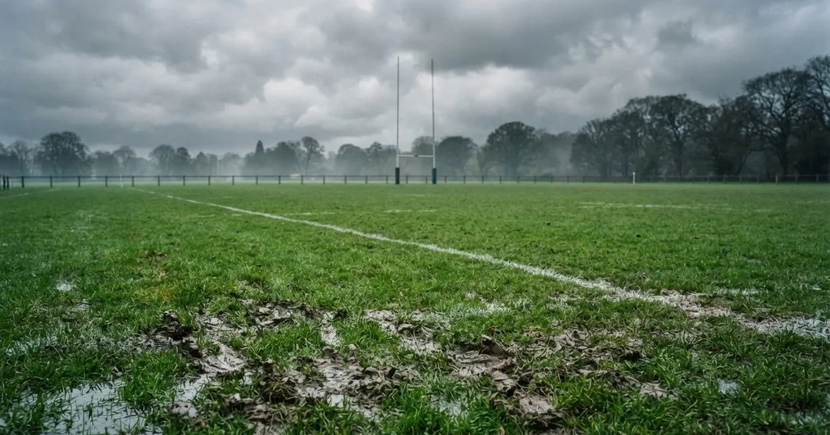 Boisko do rugby ze słupami bramki w oddali pod pochmurnym niebem, mokra trawa i ślady butów.