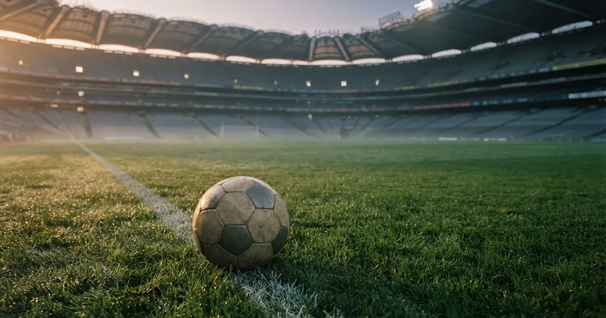 Samotna piłka na murawie ogromnego stadionu o świcie po zakończonej imprezie, trybuny puste.