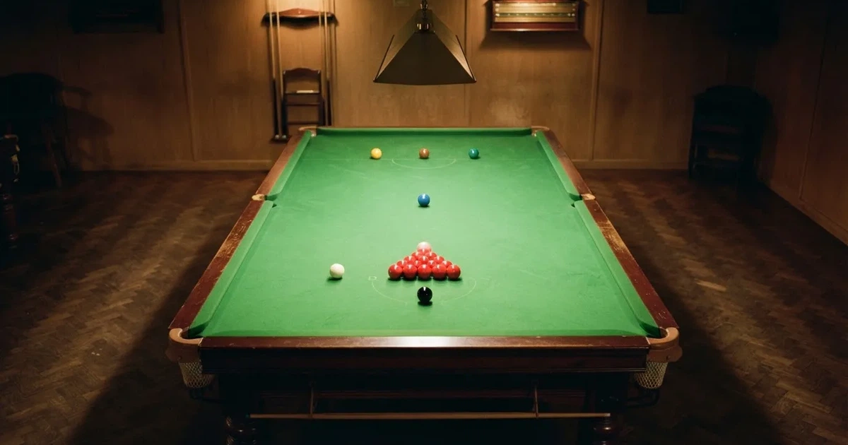 Stół snookerowy z zielonym suknem widziany z góry, rozstawione kolorowe bile w pustym salonie gry.