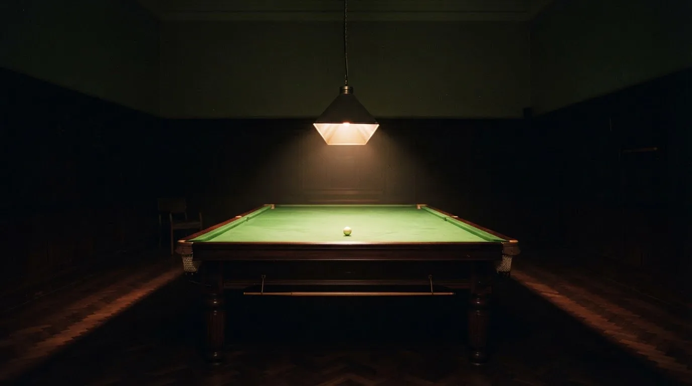 Lampa nad stołem rzuca stożek światła na zielone sukno, reszta pustego pokoju tonie w mroku.